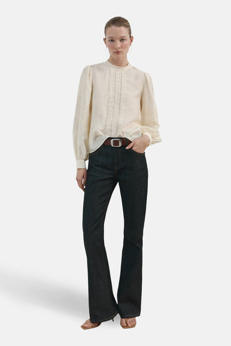 Blouse écru (manches longues) de MANGO, avec détails brodés le long du col et des manches, combinée avec un jean et une ceinture marron.
