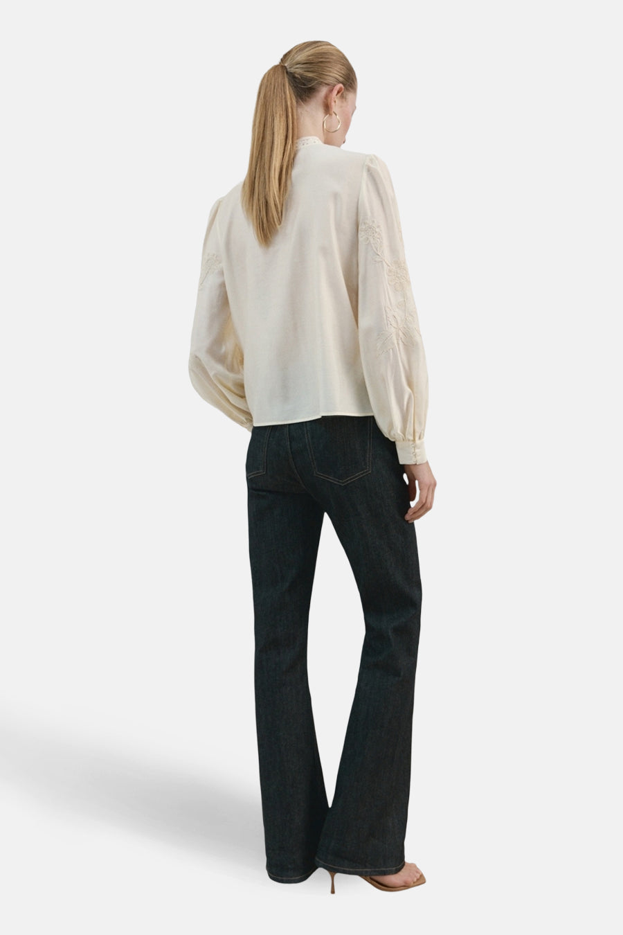 Blouse écru à manches longues de MANGO, avec détails brodés sur les manches, combinée avec un jean foncé.