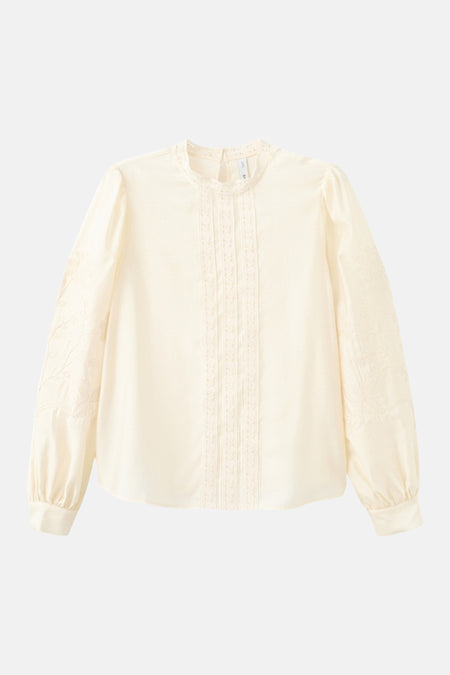 Blouse écru à manches longues de MANGO, finie avec des détails en dentelle et des broderies florales sur les manches.