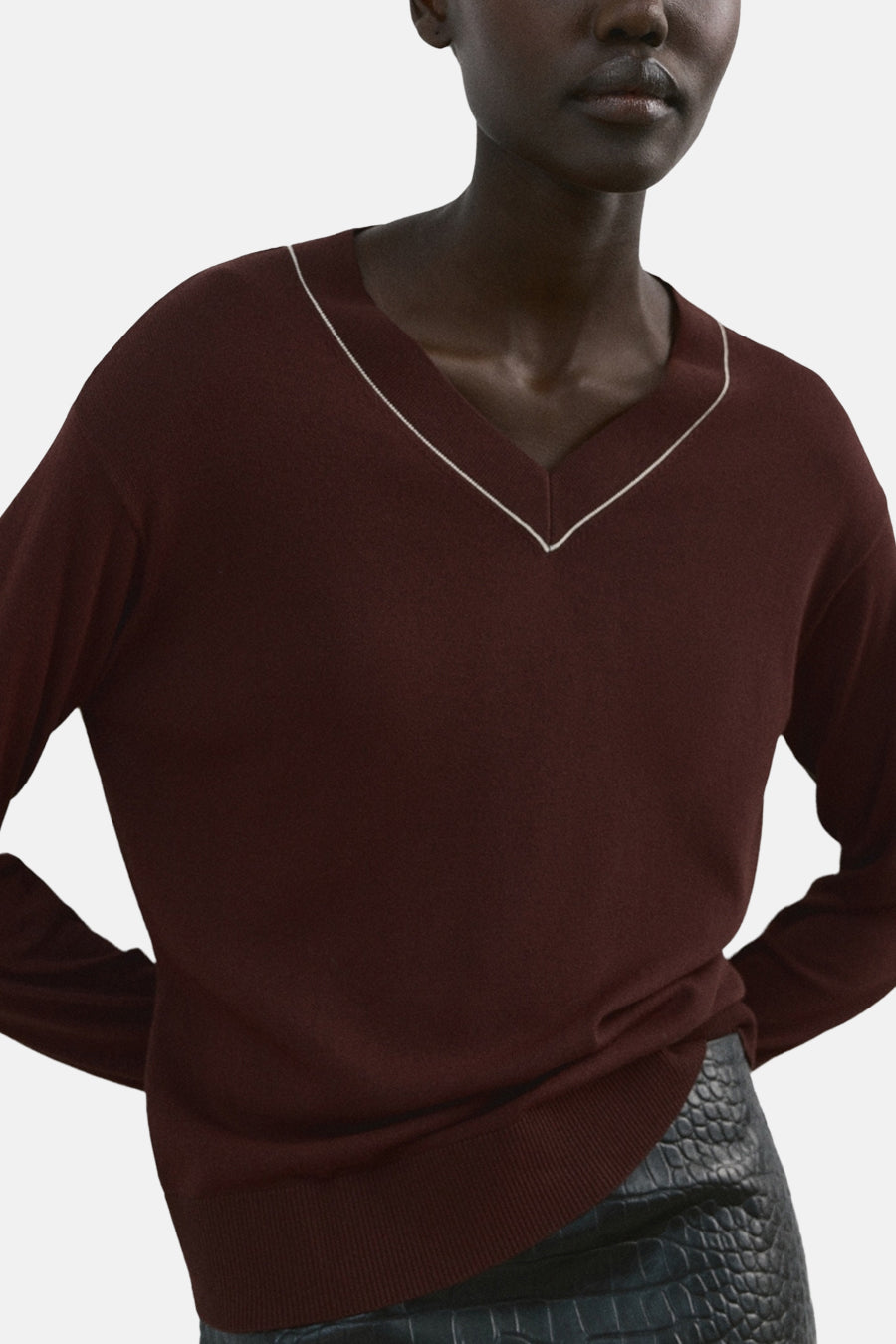 Pull marron à col en V de MANGO, avec manches longues et une mini-jupe noire ajustée à imprimé crocodile.