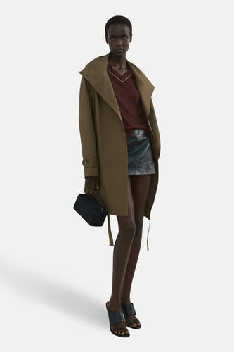Pull marron à col en V de MANGO, associé à un manteau marron et une jupe en cuir noir à imprimé crocodile.