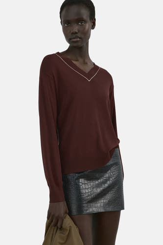 Pull marron à col en V de MANGO, avec des accents blancs le long de l'encolure, porté avec une jupe noire à imprimé crocodile.