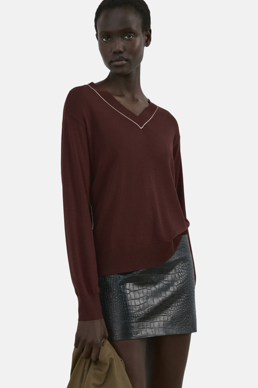 Pull marron à col en V de MANGO, avec des accents blancs le long de l'encolure, porté avec une jupe noire à imprimé crocodile.