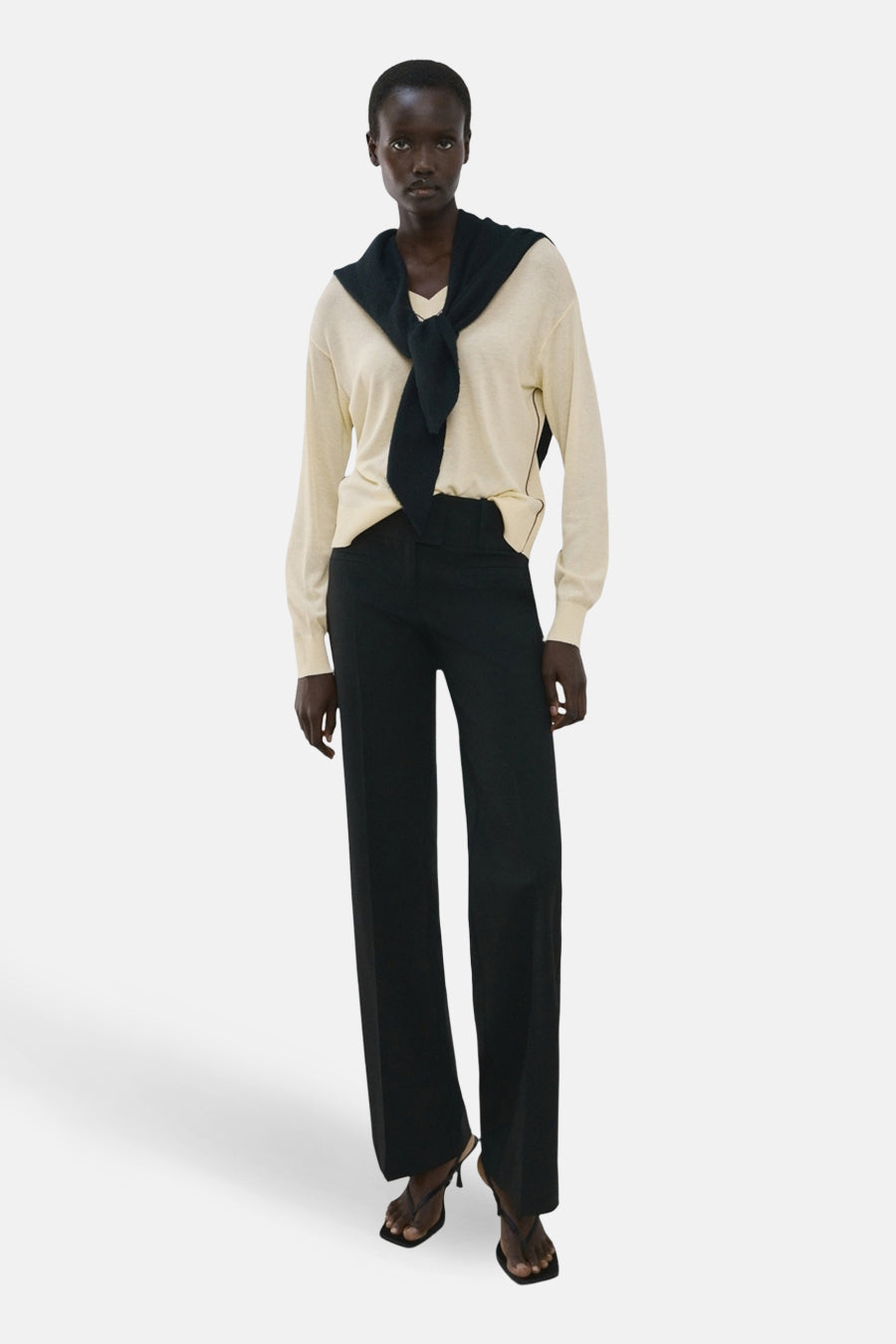 Pull jaune à col en V de MANGO, avec un pull foncé noué sur les épaules, associé à un pantalon noir droit.