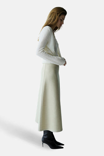 Gilet écru de MANGO, porté avec un pull blanc et une jupe beige, en vue de profil.
