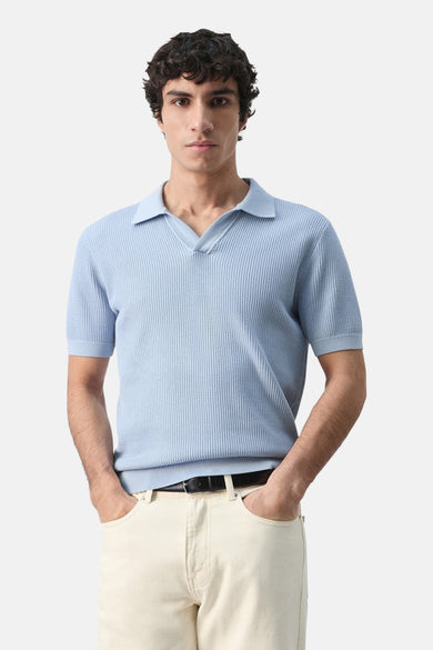 Polo bleu à manches courtes de MANGO, vue de dos, avec une texture côtelée et un pantalon de couleur crème.