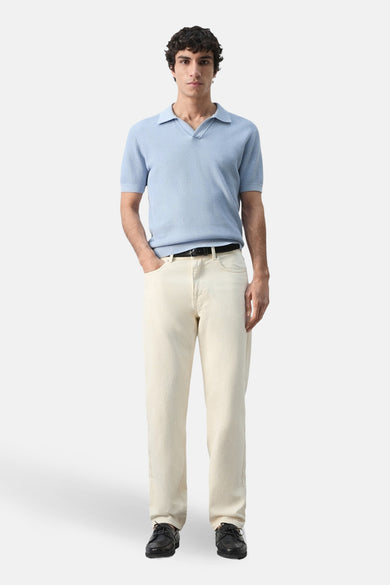 Polo bleu à manches courtes de MANGO, avec des côtes et porté avec un jean écru et des chaussures noires.