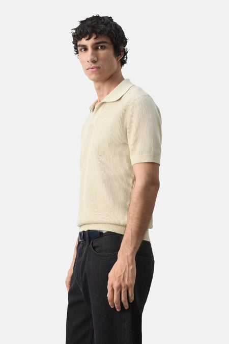 Beige korte mouwen polo van MANGO, gebreid textuur, zijprofiel, model draagt donkere jeans en riem