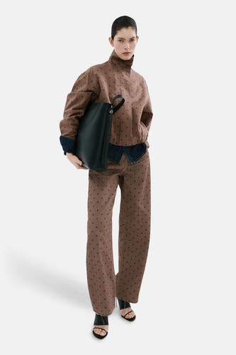Veste courte marron de MANGO, avec un motif à pois intégral et des accents en denim, combinée avec un pantalon assorti et des sandales.