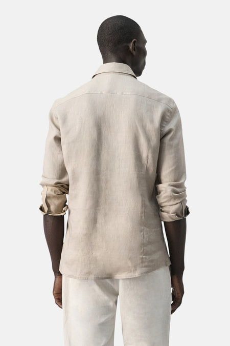 Beige linnen overhemd van MANGO, gezien van achteren, met opgerolde mouwen en lichte pantalon.
