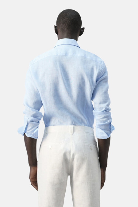 Blauw overhemd met lange mouwen van MANGO, gezien vanaf de achterkant met opgerolde mouwen en witte broek.
