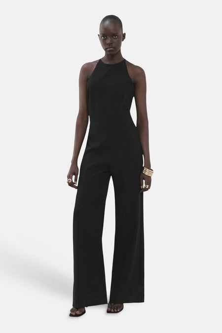 Combinaison noire de MANGO, avec encolure dos nageur et bracelets et bagues dorés comme accessoires.