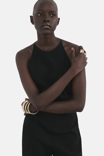 Zwarte jumpsuit van MANGO, met racerback halslijn en gouden armbanden en ringen als accessoire.