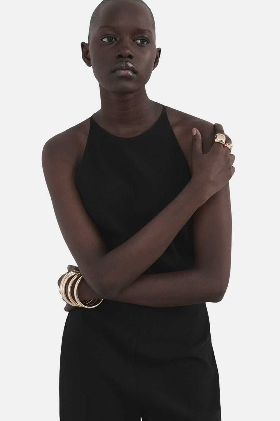 Zwarte jumpsuit van MANGO, met racerback halslijn en gouden armbanden en ringen als accessoire.