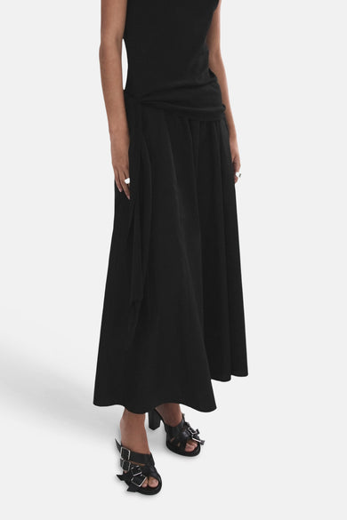 Jupe longue évasée noire de MANGO, vue de dos, portée par un mannequin avec un haut noir et des mules.