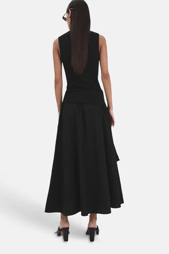 Zwarte lange wijduitlopende rok van MANGO, achterkant, gedragen door een model met zwarte top en muiltjes.