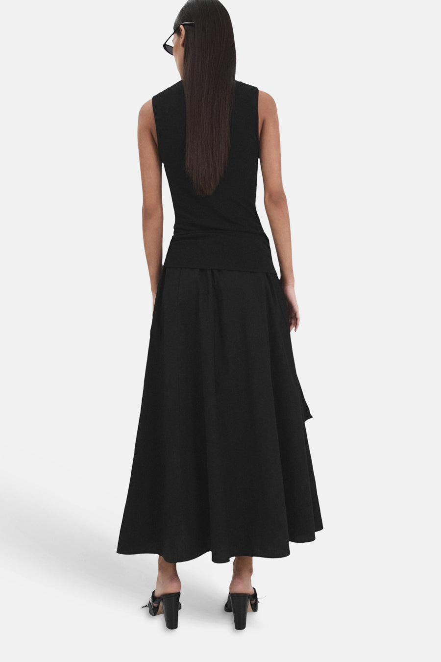 Zwarte lange wijduitlopende rok van MANGO, achterkant, gedragen door een model met zwarte top en muiltjes.