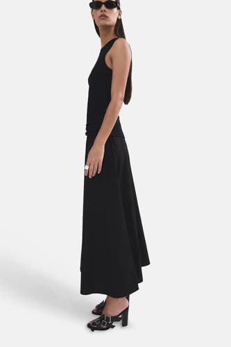 Jupe longue noire de MANGO, portée par un mannequin de profil avec un débardeur et des sandales à boucle.