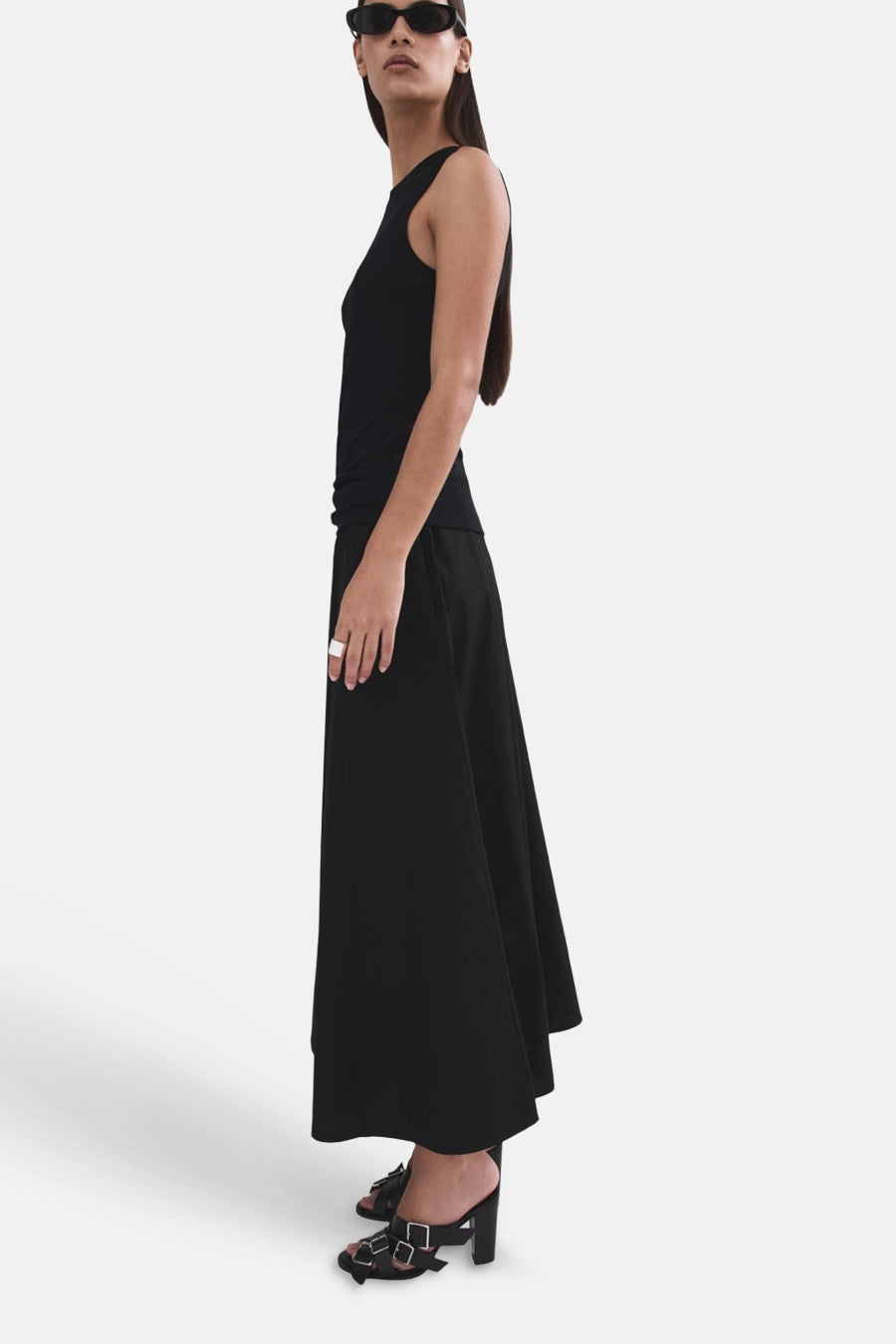Jupe longue noire de MANGO, portée par un mannequin de profil avec un débardeur et des sandales à boucle.