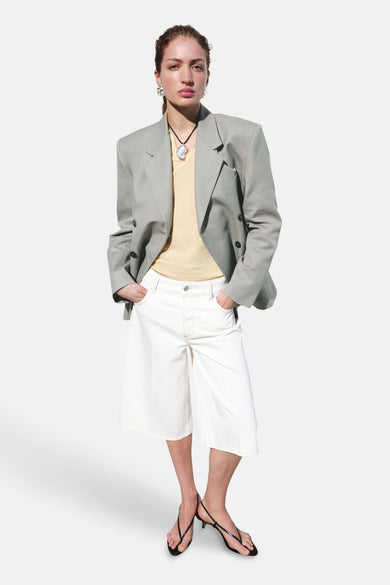 Bermuda blanche MANGO à jambes larges et coutures apparentes, portée avec un haut jaune, un blazer gris et des sandales noires.