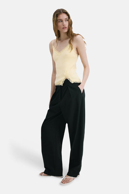 Haut à fines bretelles jaune MANGO avec détails en dentelle, combiné avec un pantalon ample foncé et des tongs claires.