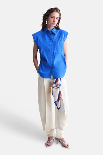 Chemise sans manches bleue de MANGO avec col et poches, combinée avec un pantalon de couleur crème.