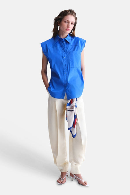 Chemise sans manches bleue de MANGO avec col et poches, combinée avec un pantalon de couleur crème.