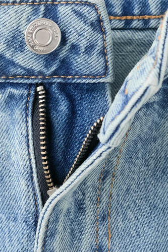 Jeans coupe droite en denim bleu clair de MANGO, avec fermeture éclair ouverte et bouton argenté.