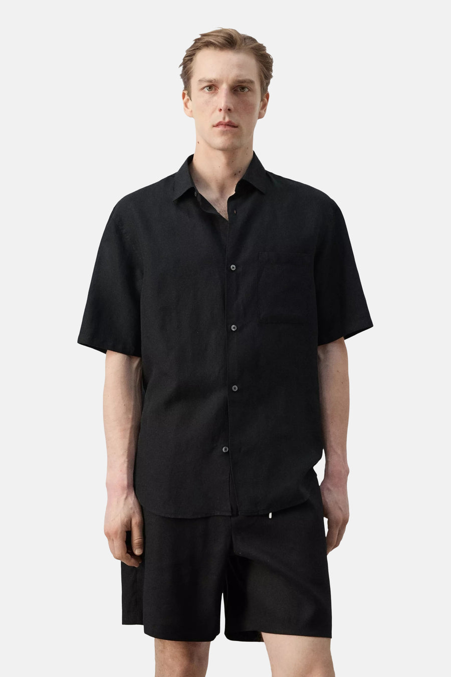 Chemise noire à manches courtes de MANGO, vue de dos, coupe ample et texture légère, portée avec un short noir.