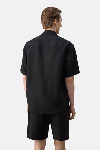 Zwart hemd met korte mouwen van MANGO, van achteren gezien, met losse pasvorm en lichte textuur, gedragen met zwarte korte broek.