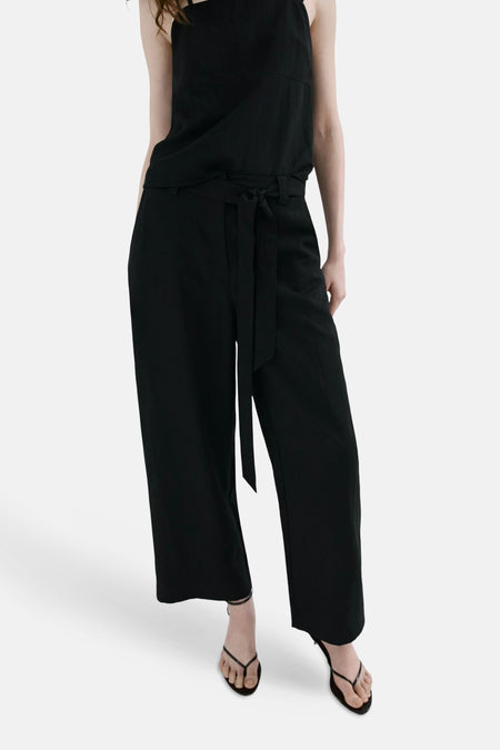 Pantalon noir ample de MANGO, vu de dos, porté avec un haut noir et des sandales.