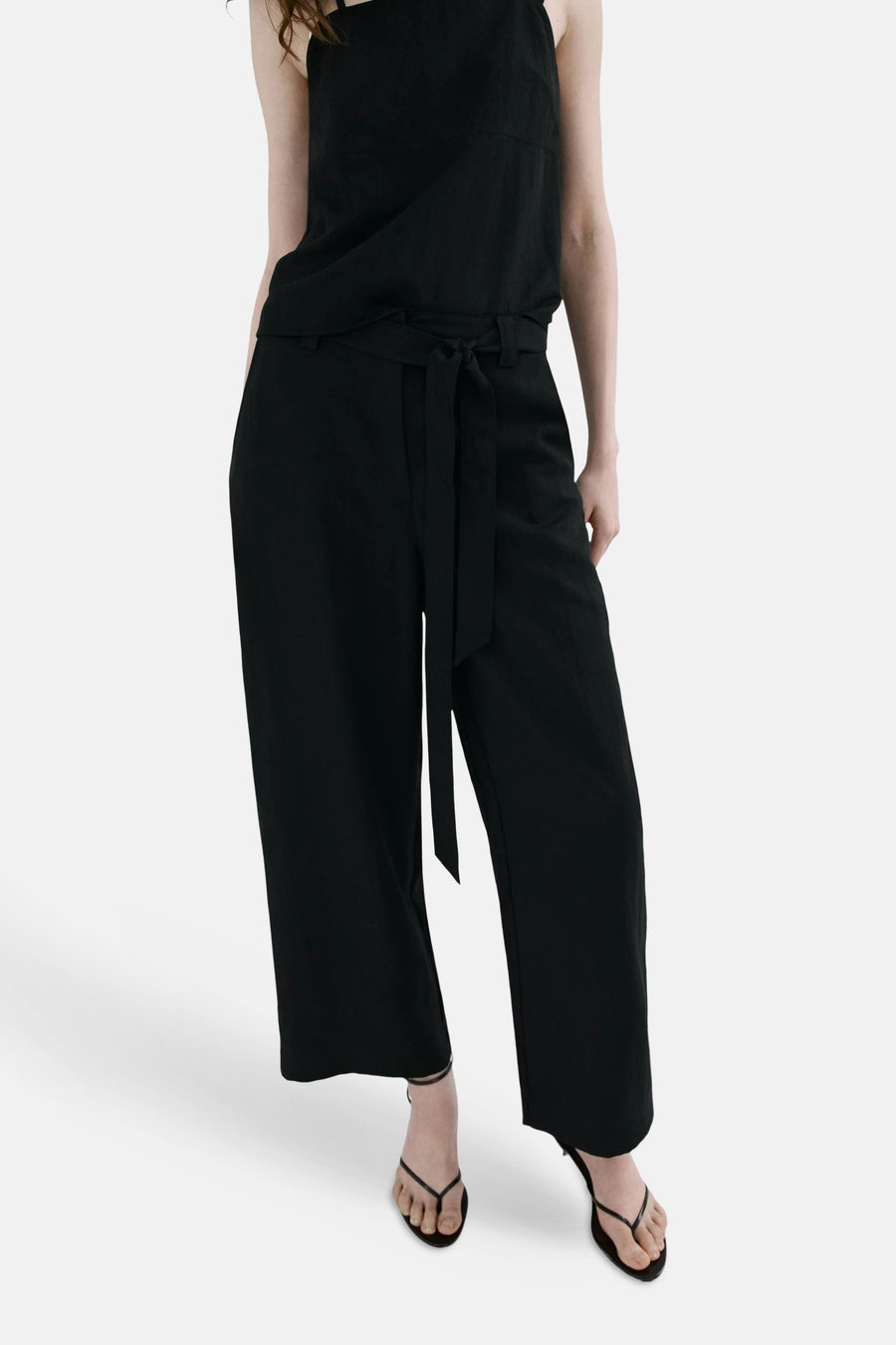 Pantalon noir ample de MANGO, vu de dos, porté avec un haut noir et des sandales.