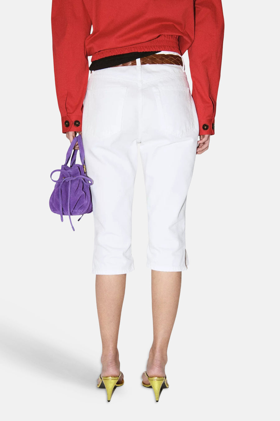 Witte 5-pocket capribroek van MANGO, van achteren gezien met zijsplitten onderaan. Gedragen met een rood overhemd en paarse suède tas.