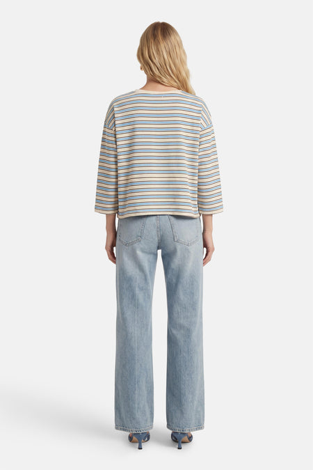 T-shirt bleu rayé (manches longues) de Terra di Siena, avec des accents beiges et une coupe droite, combiné avec un jean denim clair et des talons bleus.