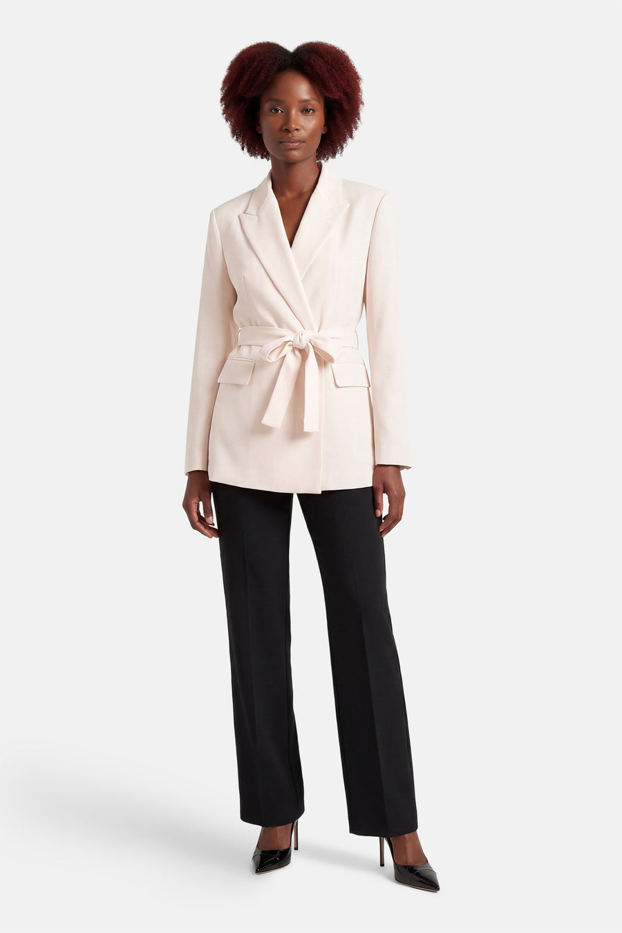 Ecru blazer van MANGO met een geknoopte tailleband, gedragen met zwarte pantalon en hakken.
