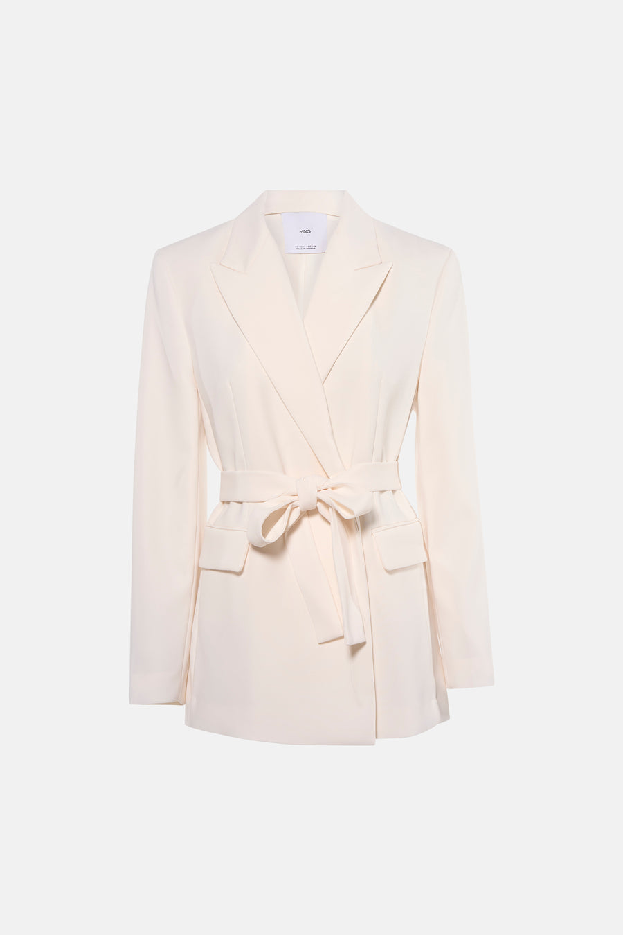 Blazer écru de MANGO, avec ceinture et porté avec un pantalon noir et des talons hauts.