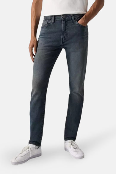 Tapered jeans in donkergrijs denim van Levi's, met witte sneakers en een witte top.
