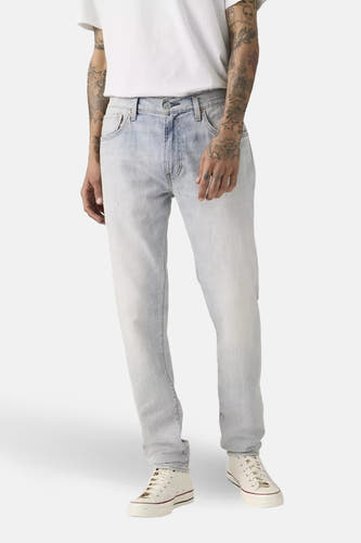 Jeans fuselés en denim bleu clair de Levi's, portées avec un t-shirt blanc et des baskets couleur crème, en vue de côté.