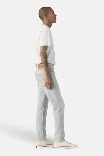 Jeans tapered van lichtblauw denim van Levi's, gedragen met een wit T-shirt en crèmekleurige sneakers, in zijaanzicht.
