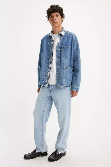 Jean droit bleu clair de Levi's, avec des jambes larges, associé à un T-shirt blanc et à des chaussures noires, en vue latérale.