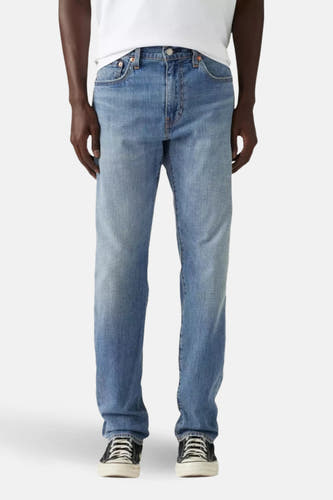 Jean tapered bleu clair de Levi's, avec un patch en cuir marron et porté avec un T-shirt blanc et des baskets noires.