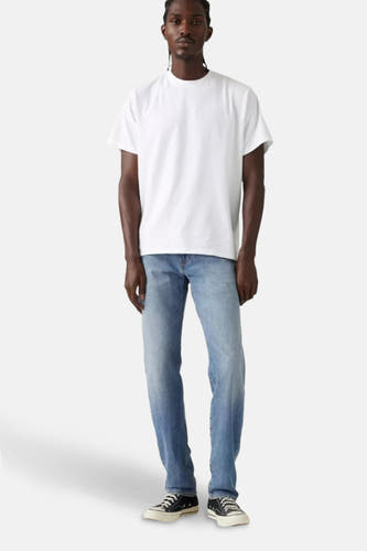 Lichtblauwe tapered jeans van Levi's®, gedragen met een wit T-shirt en zwarte sneakers.
