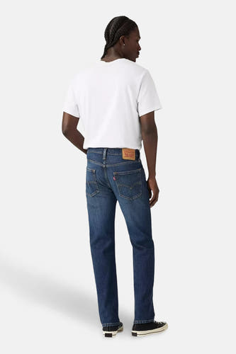 Jean tapered en denim bleu marine de Levi's, vu de de derrière, associé à un t-shirt blanc et des chaussures noires.