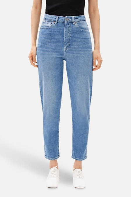 Jean mom bleu moyen d'ARMED ANGELS, avec une taille haute et des jambes droites, associé à des chaussures blanches.