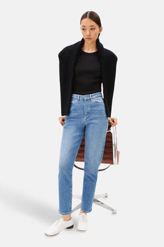 Mairaa mid blue denim mom jeans d'Armed Angels, associées à une chemise noire et un gilet, et des chaussures blanches.