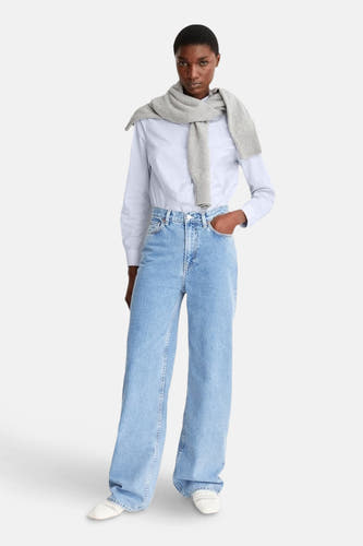 Jean bleu clair large d'ARMED ANGELS, associé à un chemisier bleu clair et une veste grise sur les épaules.