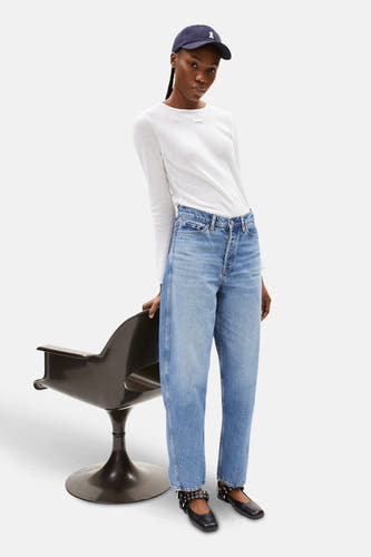 Jean denim bleu marine spécial fit d'ARMEDANGELS, porté avec un t-shirt blanc, des ballerines noires et une casquette de baseball bleue.