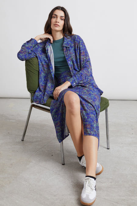 Chemise bleue à manches longues de 24 couleurs, avec un motif coloré, portée sur une chemisier verte et une jupe coordonnée.