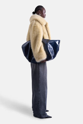 Manteau court bleu de TOPSHOP, porté avec une grande sacoche en cuir bleu et des jeans gris larges, photographié sur le côté.