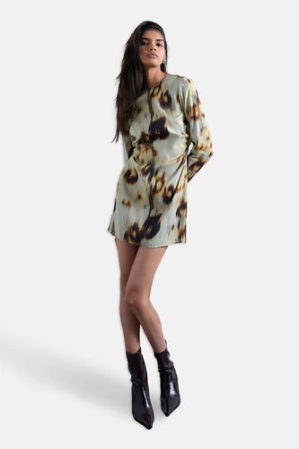 Vrouw in bedrukte jurk en zwarte laarzen, staand voor witte achtergrond.
